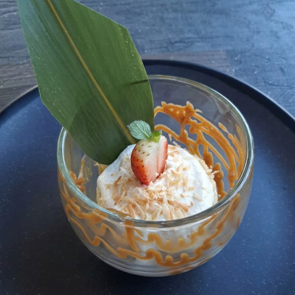 Coconut ice cream with caramel drizzle, toasted coconut flakes, a strawberry, and mint in a glass.